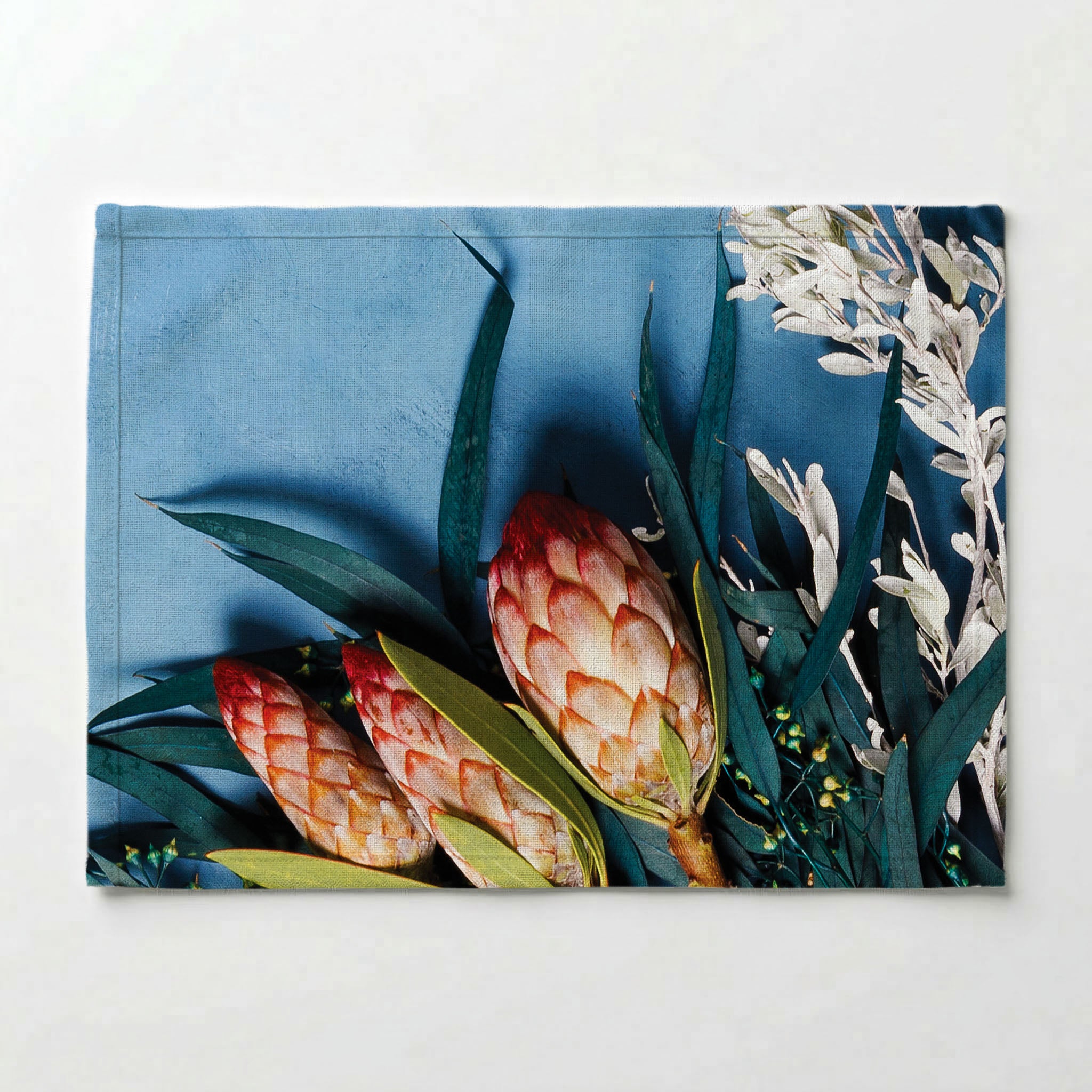 PINK PROTEAS WITH EUCALYPTUS ON BLUE PLACEMAT